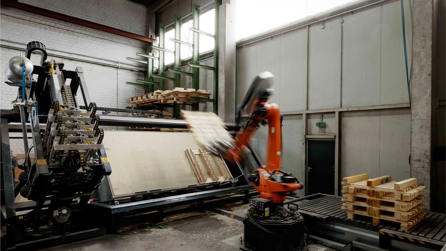 Roboterarm legt fertige Paletten auf Förderband ab.