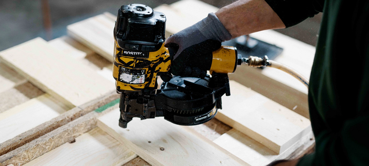 Pneumatic nailer being applied to a wooden frame.