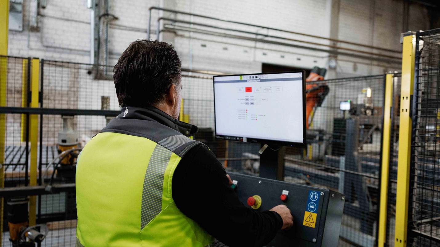 Mitarbeiter mit Warnweste bedient das Terminal der Palettenfertigungsmaschine.