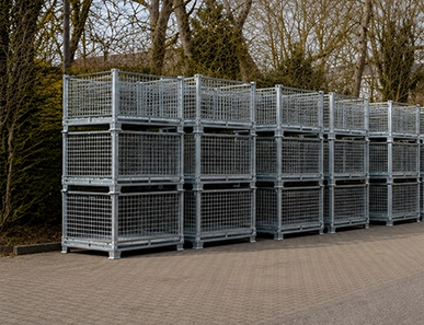 Stackable metal wire mesh boxes in the outdoor warehouse next to stacked wooden pallets.