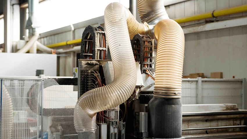 CNC‑Bearbeitungszentrum in der Werkhalle mit großen Absaugschläuchen.
