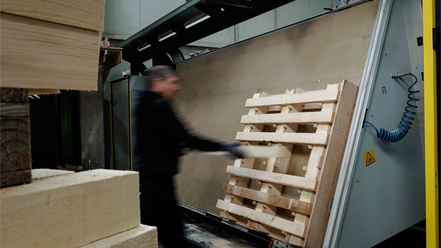  Mitarbeitender legt Holzteil in Palettenvorrichtung ein