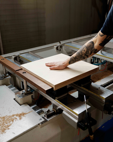 Hand legt eine Holzplatte auf den Tisch einer CNC‑Fräse.