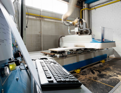 Steuerkonsole mit Tastatur im Vordergrund, CNC‑Maschine im Hintergrund in der Werkhalle.