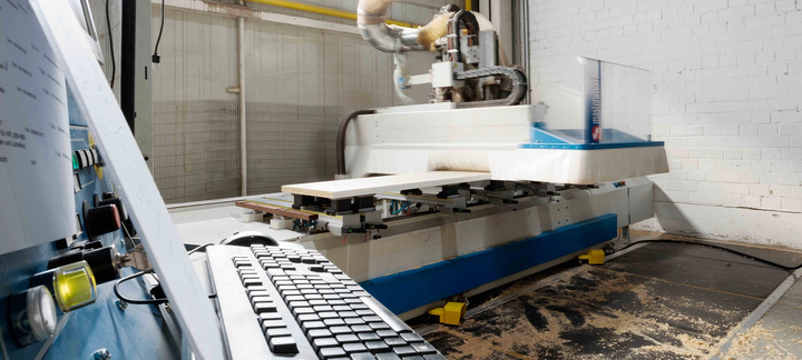 Control console with keyboard in the foreground, CNC machine in the background in the factory hall.