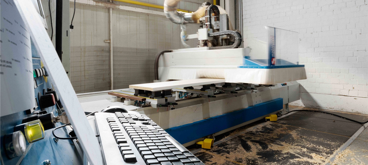 Steuerkonsole mit Tastatur im Vordergrund, CNC‑Maschine im Hintergrund in der Werkhalle.