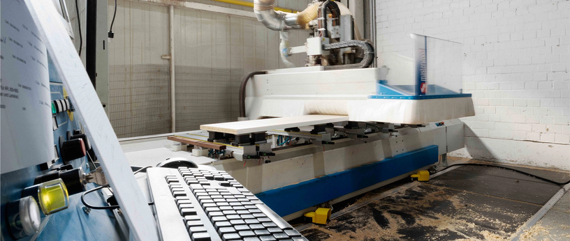 Steuerkonsole mit Tastatur im Vordergrund, CNC‑Maschine im Hintergrund in der Werkhalle.