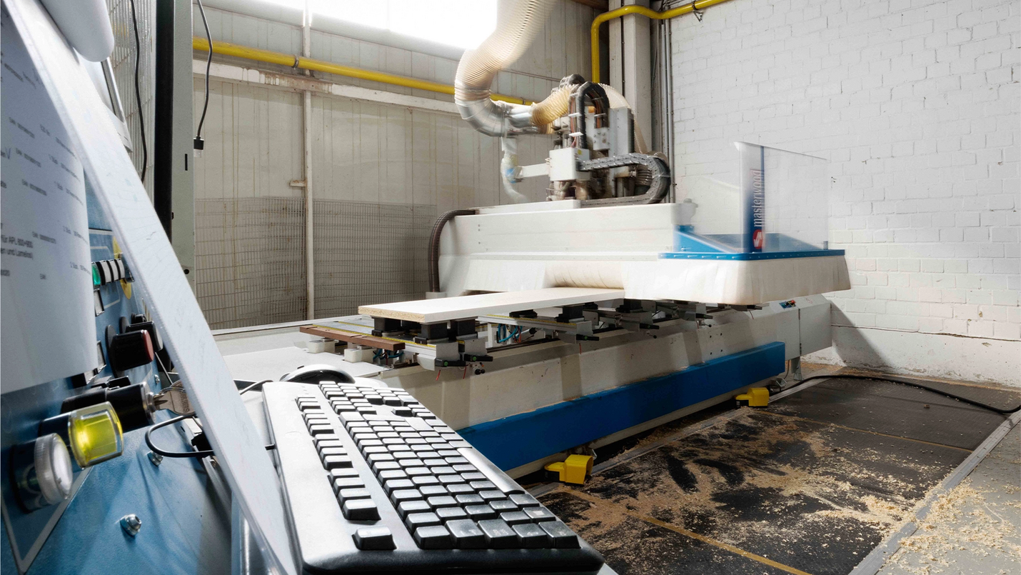 Steuerkonsole mit Tastatur im Vordergrund, CNC‑Maschine im Hintergrund in der Werkhalle.