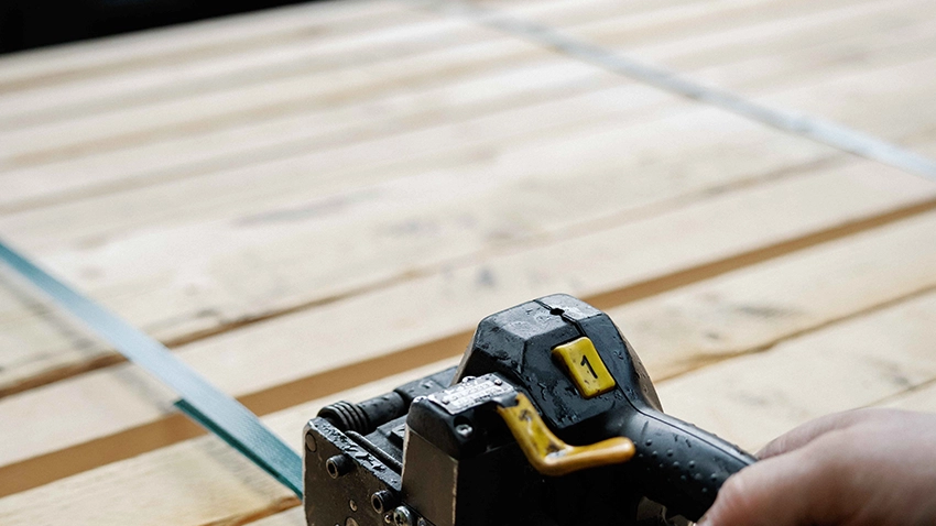 Handumreifungsgerät spannt ein Band um Holzpaket.