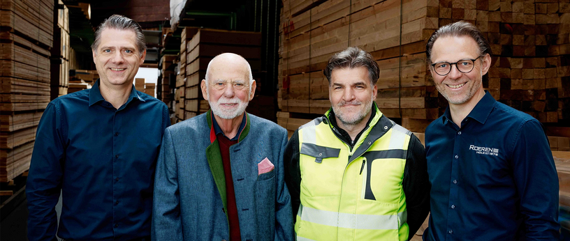 Management team of Roeren Holzdienstleistungsgesellschaft in front of stacked timber in the warehouse.