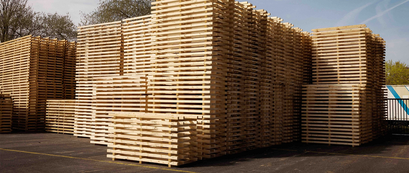 Hohe Stapel aus Holzpaletten im Außenlager bei Tageslicht.
