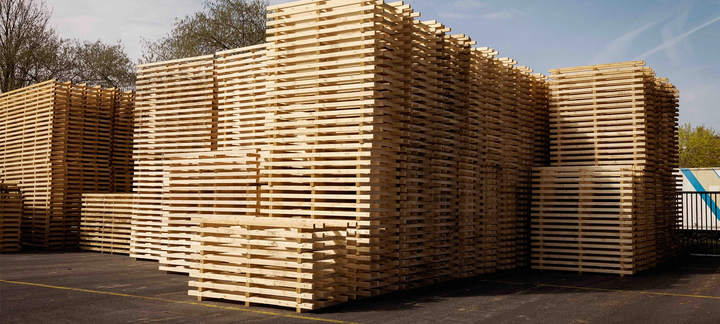 Hohe Stapel aus Holzpaletten im Außenlager bei Tageslicht.