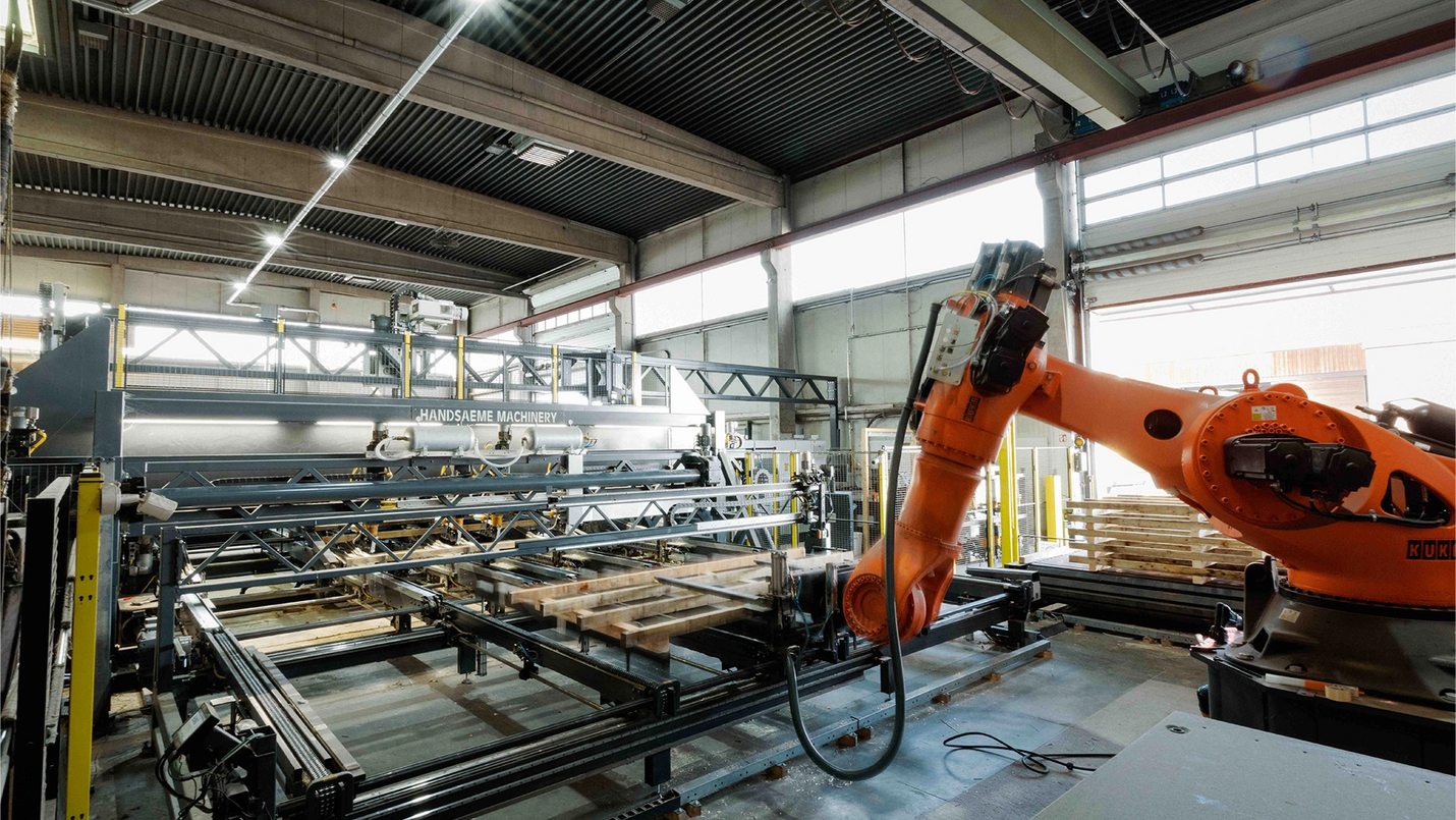 Palettenfertigungsmaschine mit Roboterarm in der Produktionshalle.