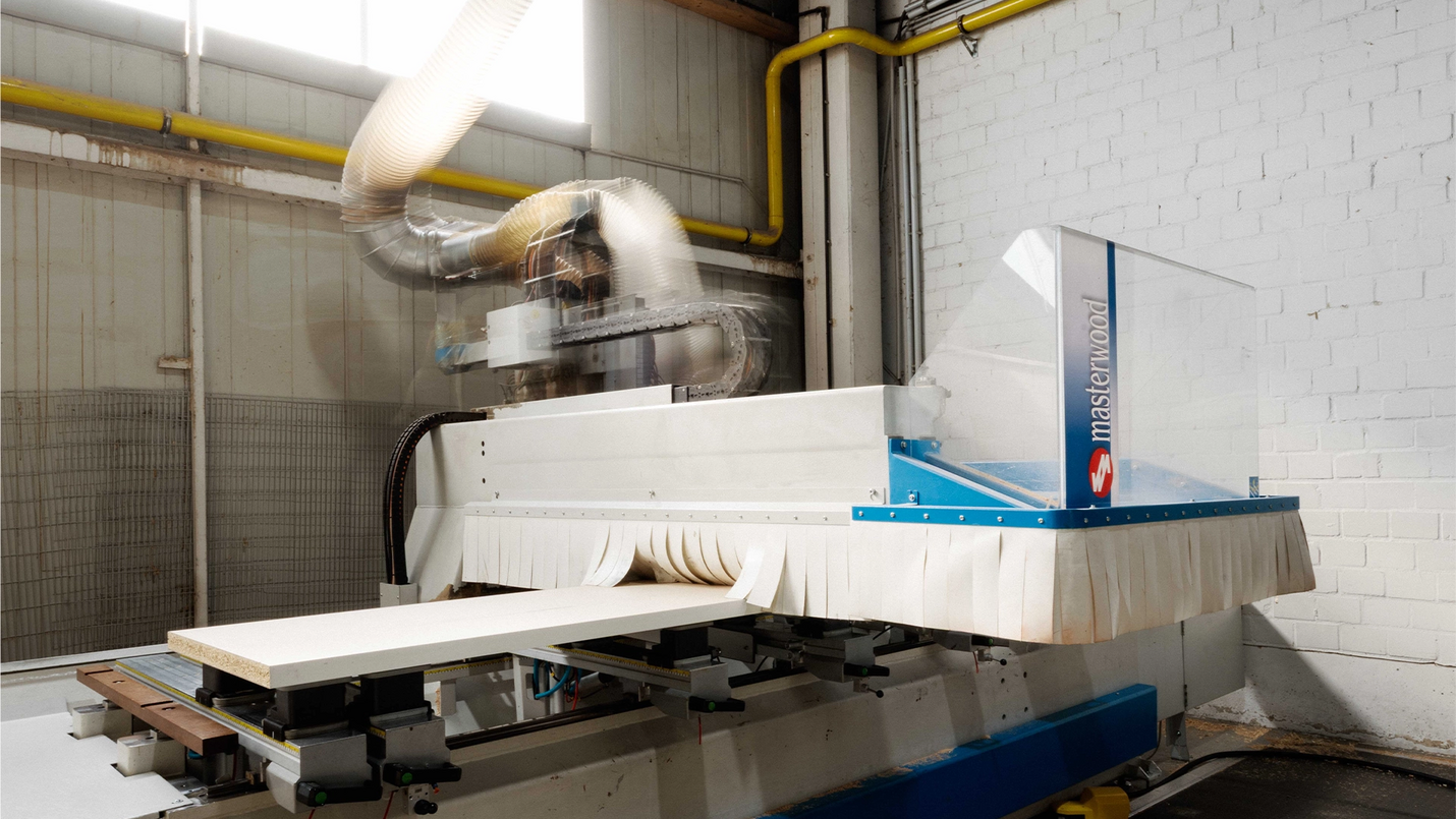 CNC‑Bearbeitungszentrum mit aufliegender Holzplatte und Absaugung in der Werkhalle.