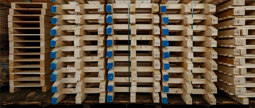 Gestapelte Palettenbauteile im Lager, Stirnseiten blau markiert.