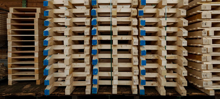 Gestapelte Palettenbauteile im Lager, Stirnseiten blau markiert.