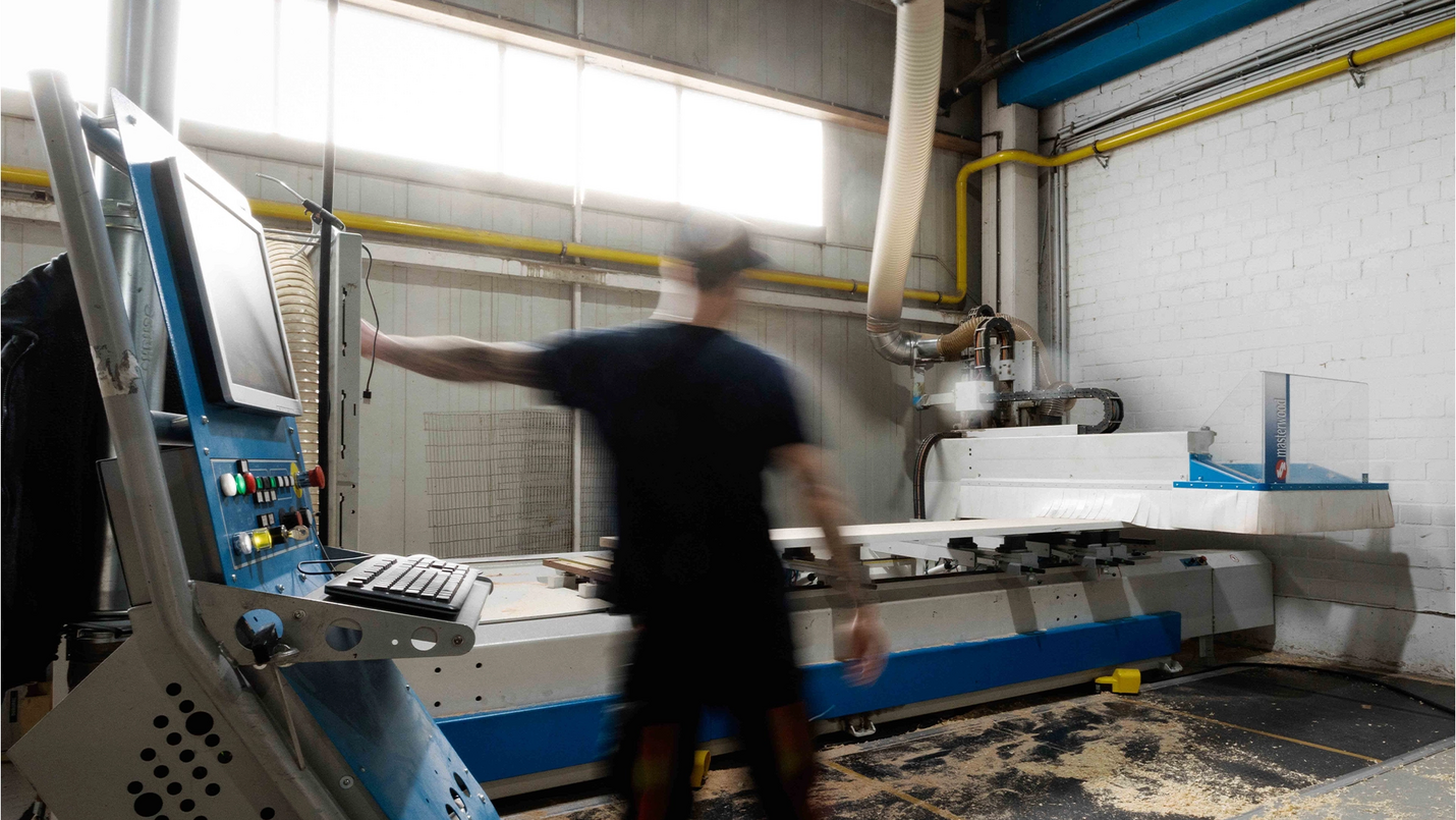 Mitarbeiter bedient eine CNC‑Maschine an der Steuerkonsole in der Werkstatt.